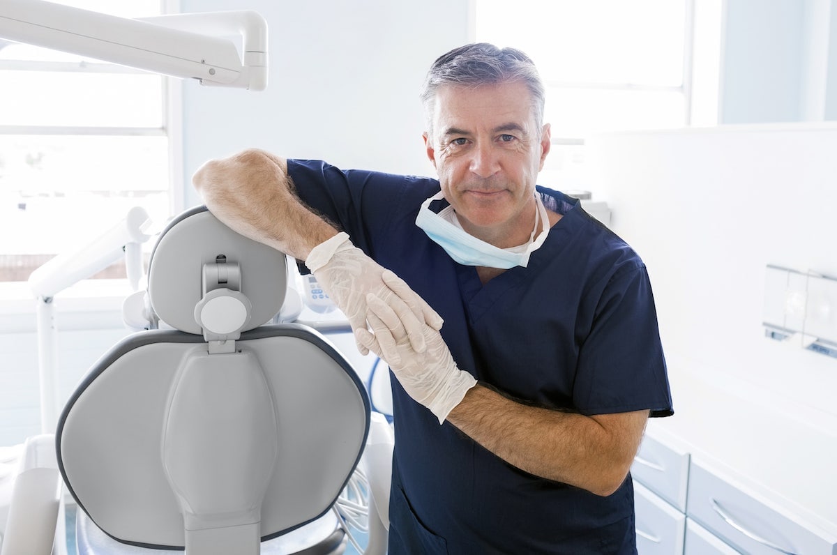Zahnarzt lehnt sich auf einen Zahnarztstuhl und lächelt